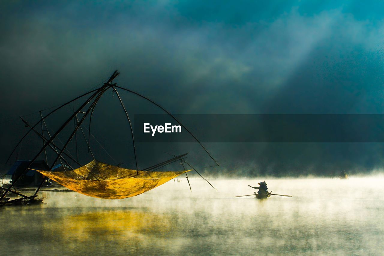 People in boat on lake by fishing net during foggy weather
