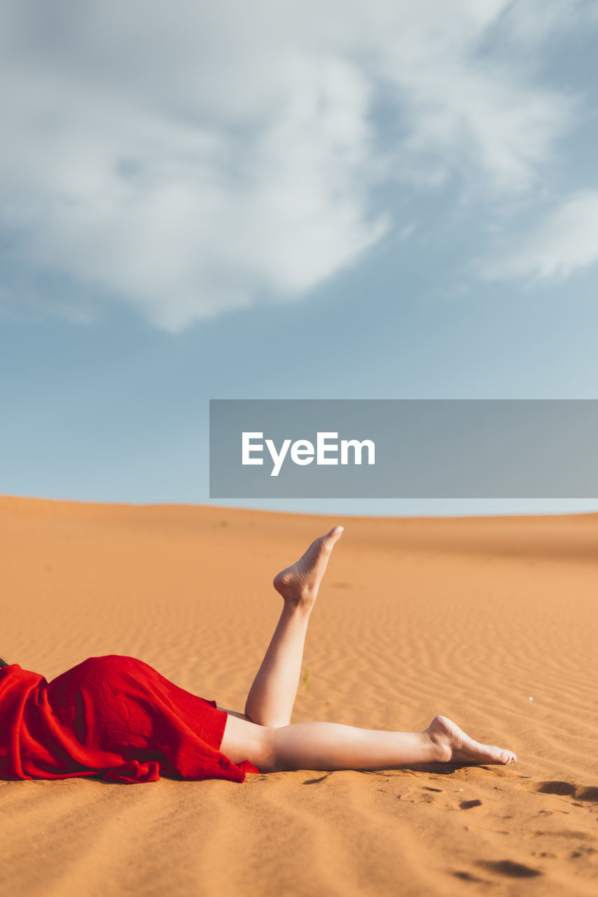 Woman lying on sand dune in desert against sky
