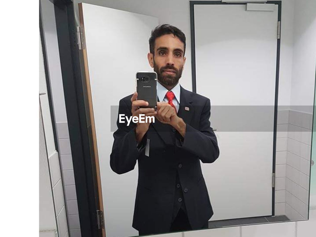 PORTRAIT OF YOUNG MAN USING MOBILE PHONE IN OFFICE