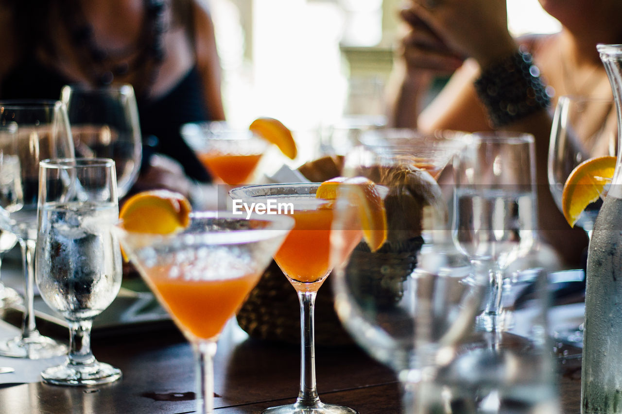 Midsection of friends sitting by martinis on table at restaurant