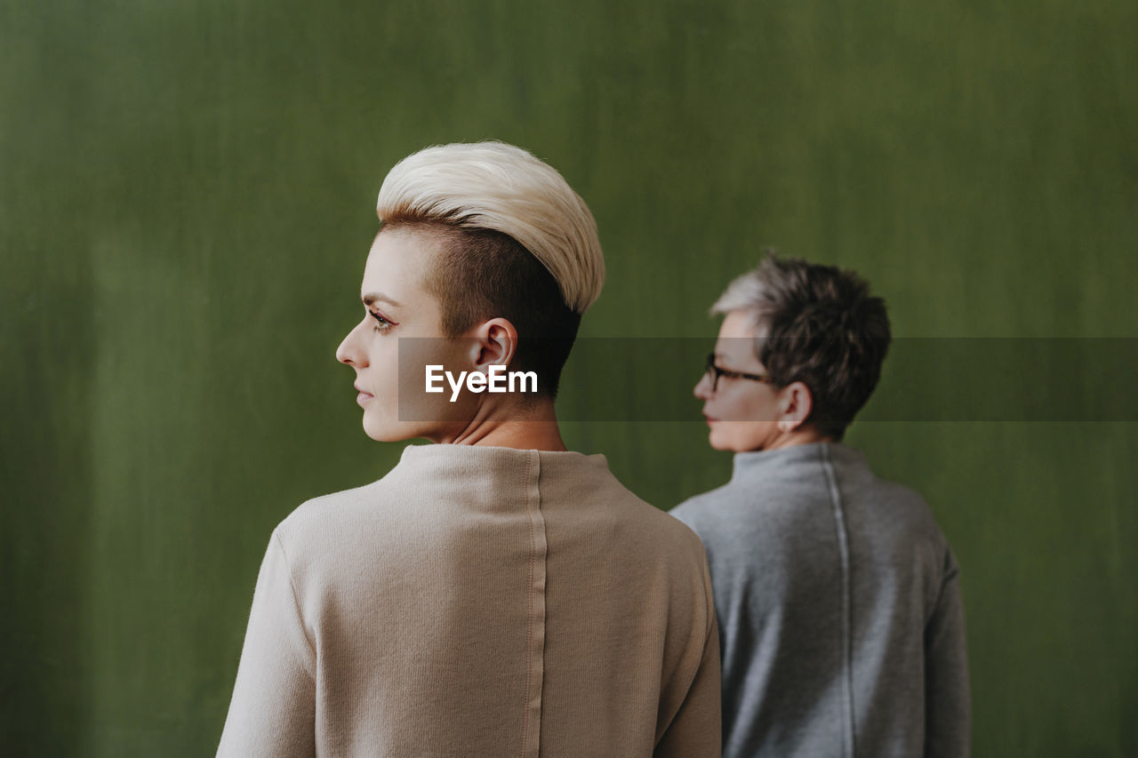 Young woman with dyed hair and mother standing in front of green wall