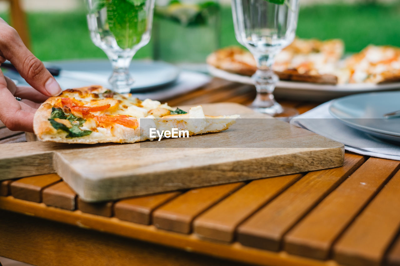 Cropped hand holding pizza slice on cutting board