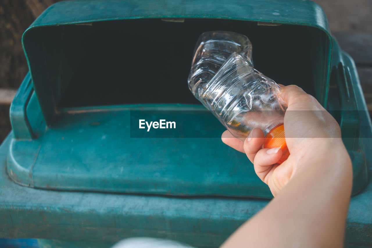 Close-up of hand putting bottle in dustbin