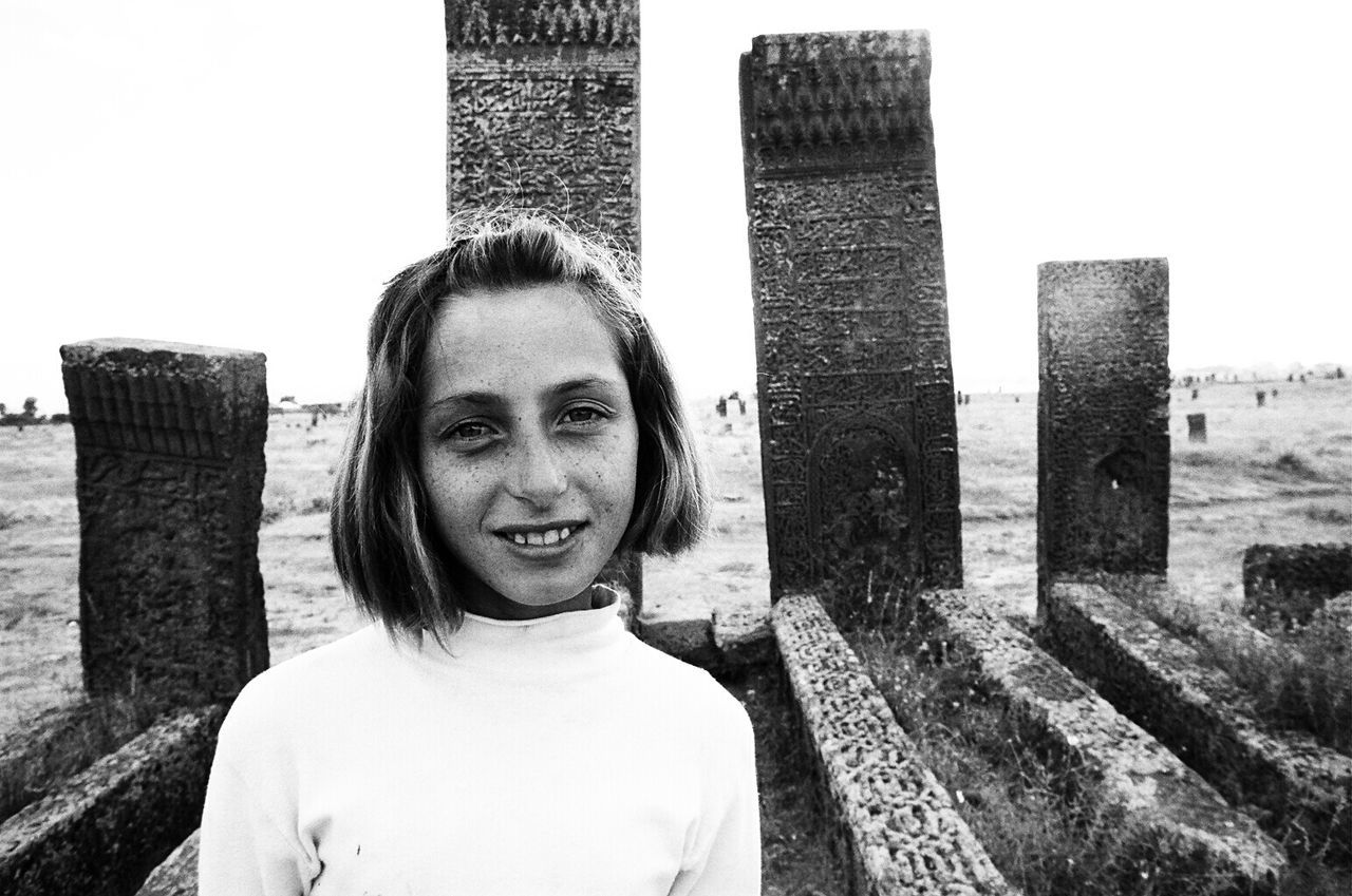 PORTRAIT OF YOUNG WOMAN STANDING BY WALL