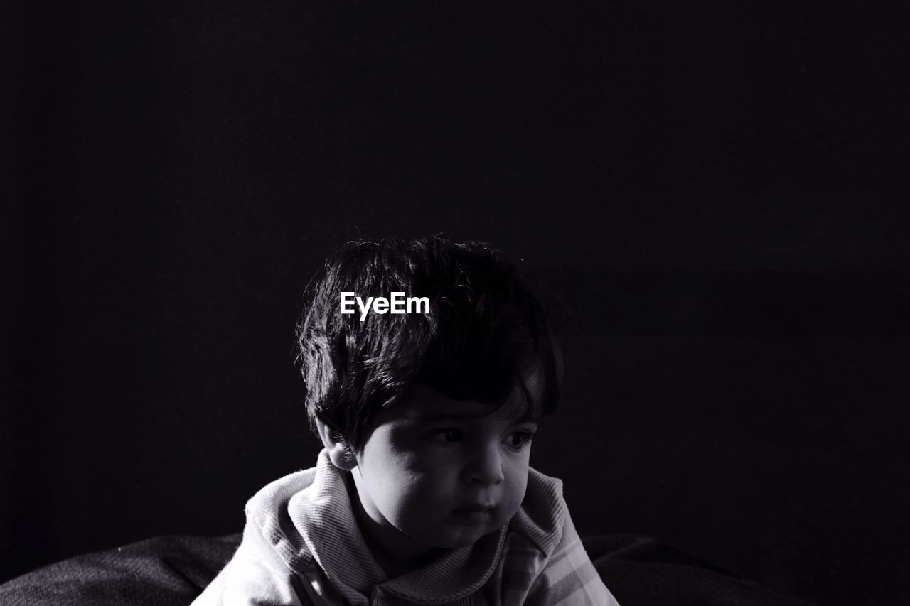 Close-up of cute boy looking down over black background