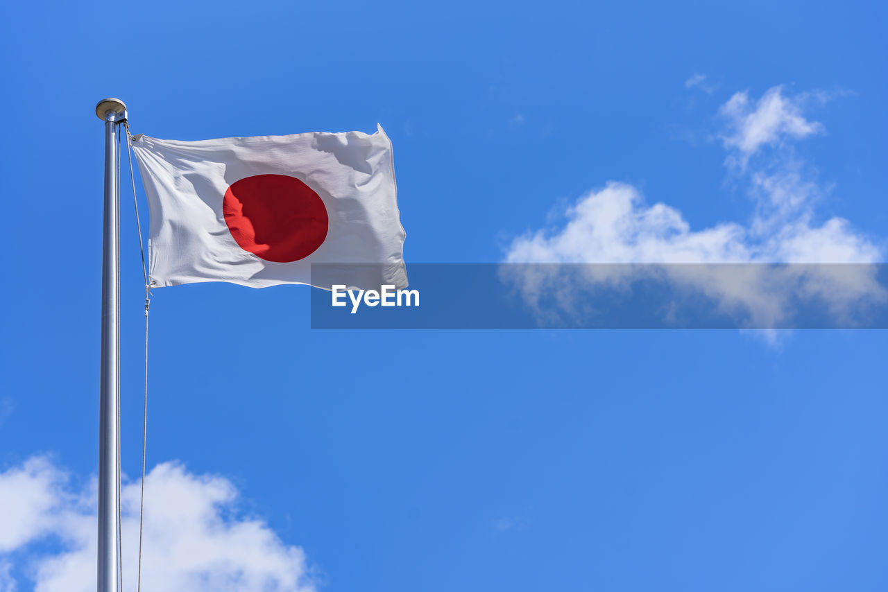 Japanese national flag waving in the wind against a sunny blue sky.