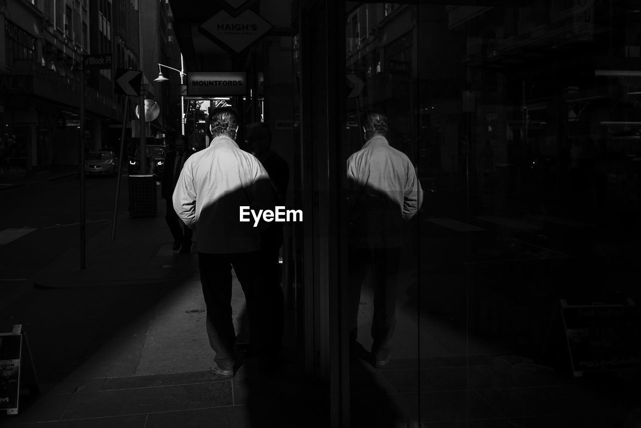 Rear view of man walking on street by glass building