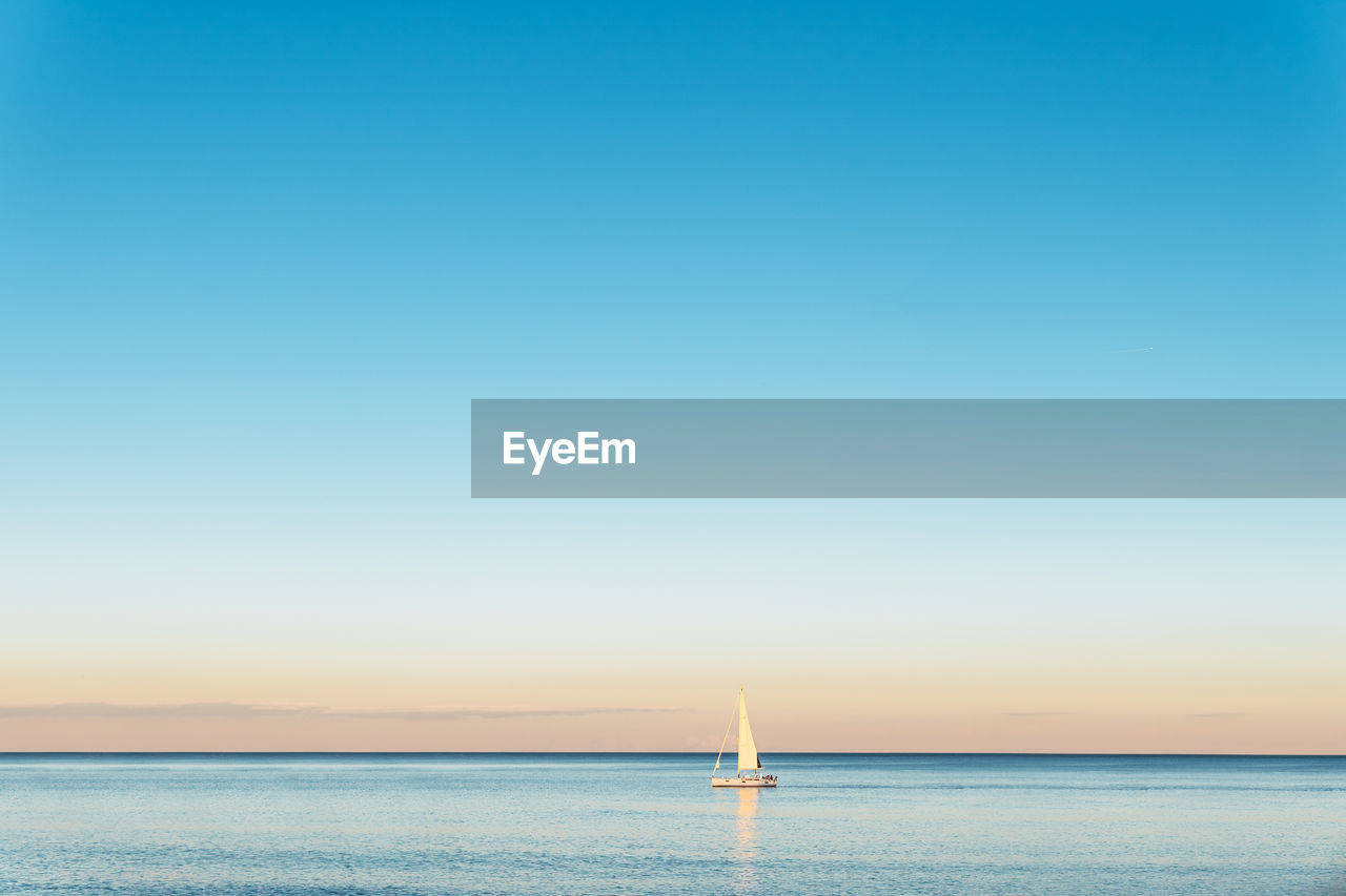 Scenic view of sailboat on rippled ocean with horizon under bright sky in daylight