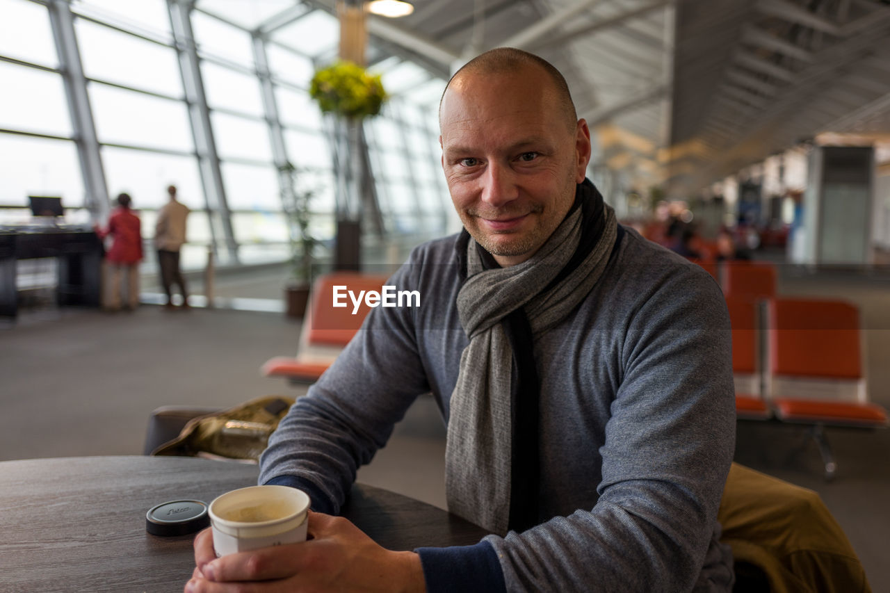 Portrait of smiling man holding disposable coffee cup while sitting at chubu centrair international airport