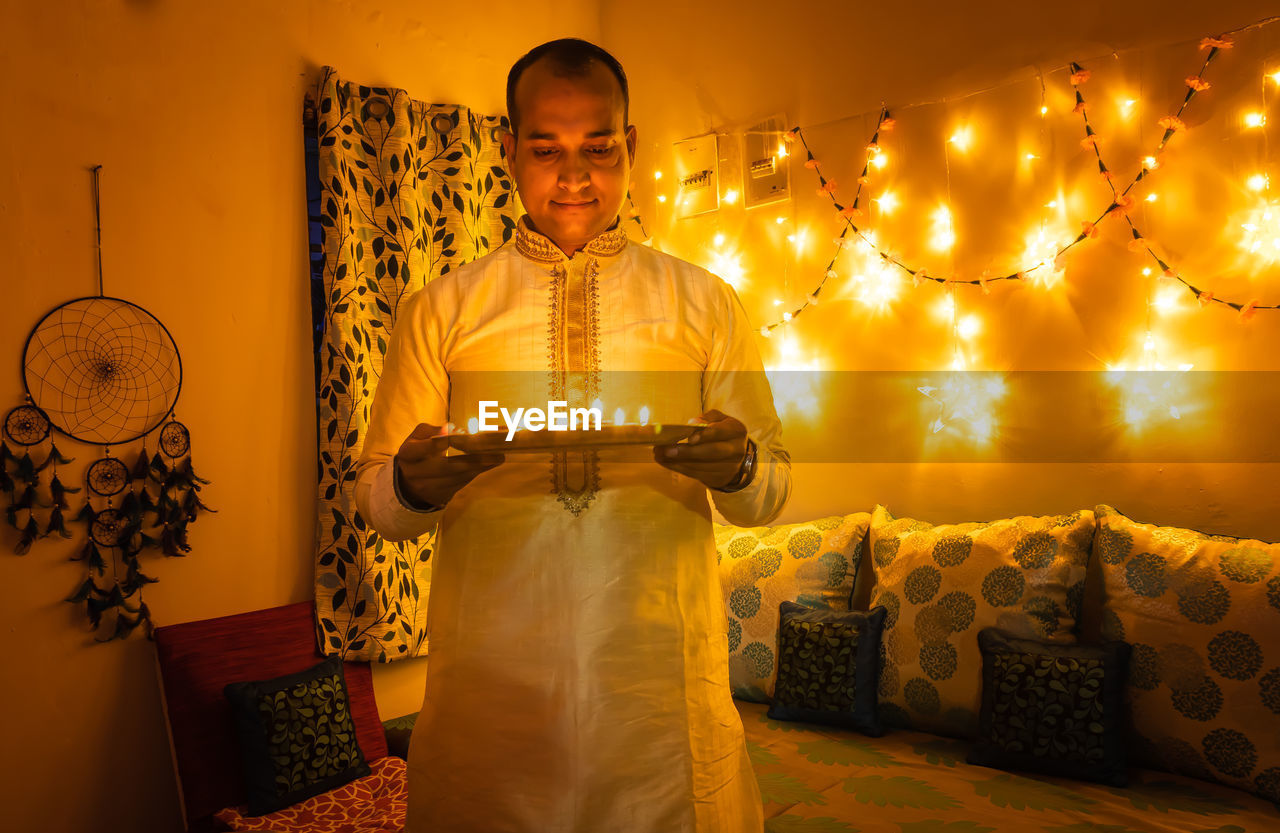 Young man in traditional dress holding the plat fill with oil lamps with ferry lights background