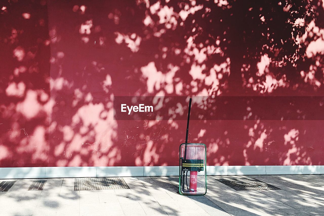 Riot shield and fire extinguisher on sidewalk against red wall