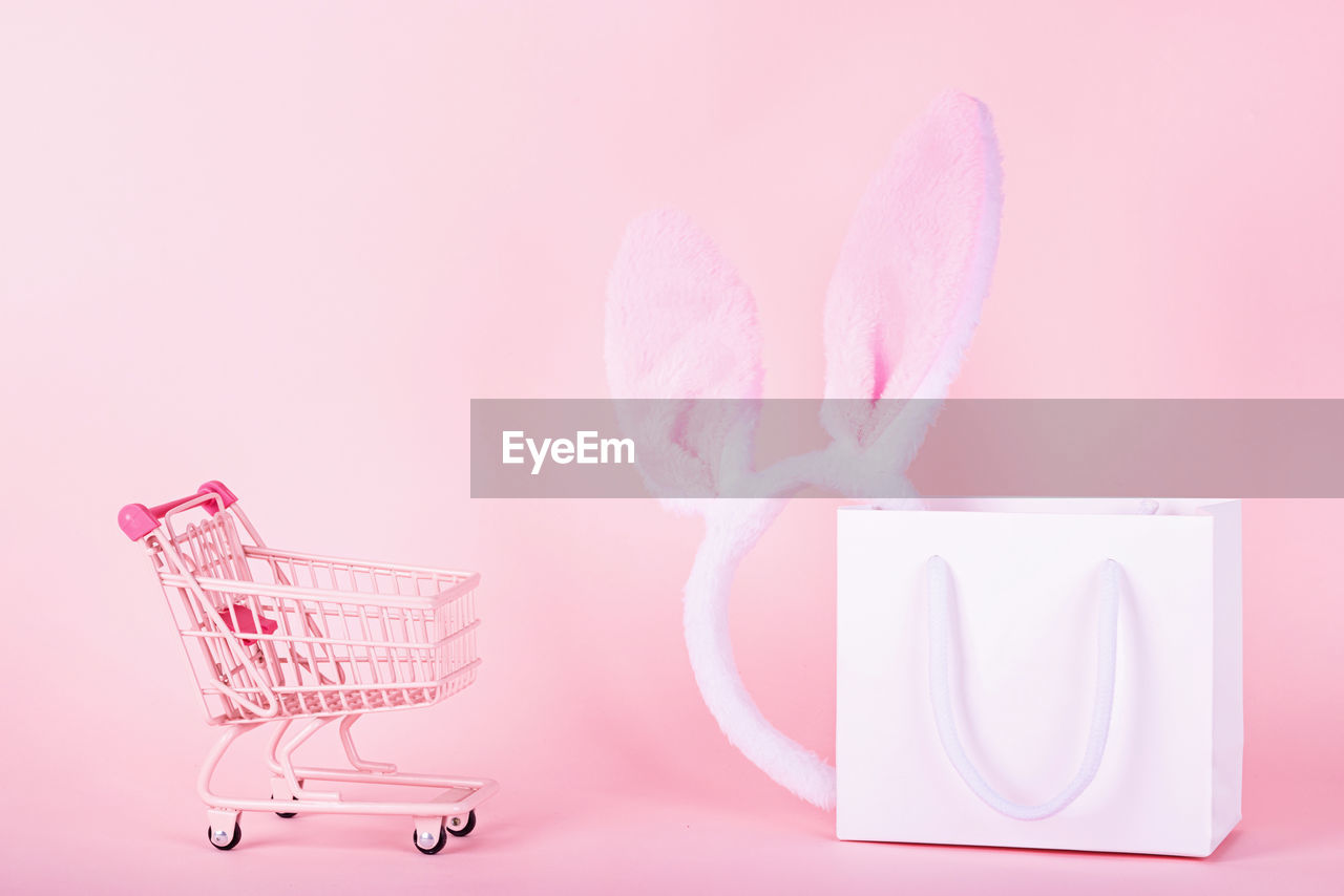 Mini shopping cart with bag against pink background