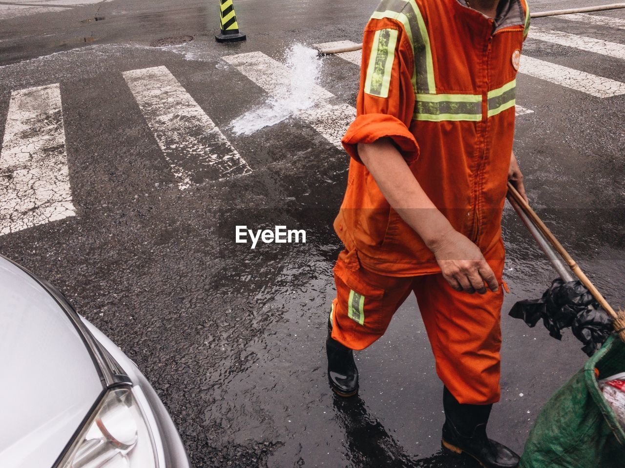 Low section of manual worker walking on wet street during rainy season