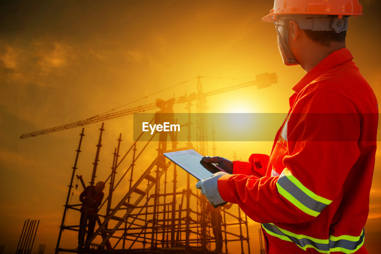 Man working at construction site against sky during sunset