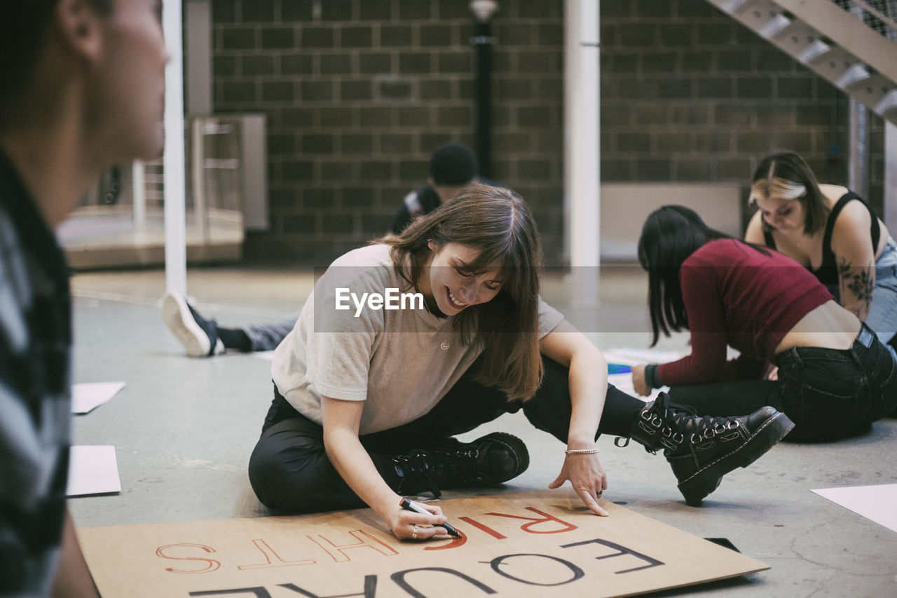 Smiling woman preparing signboard while sitting with male and female activists in building