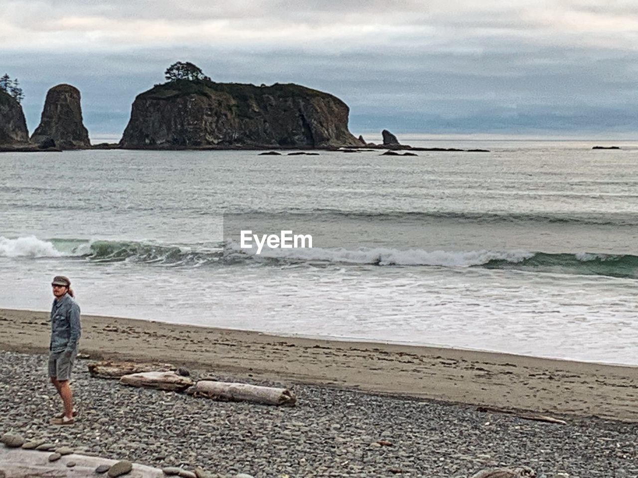 MAN STANDING ON ROCKS AT BEACH AGAINST SKY