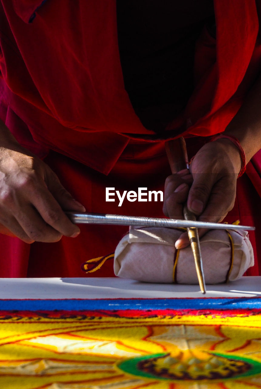 Midsection of woman using chak-pur for sand painting