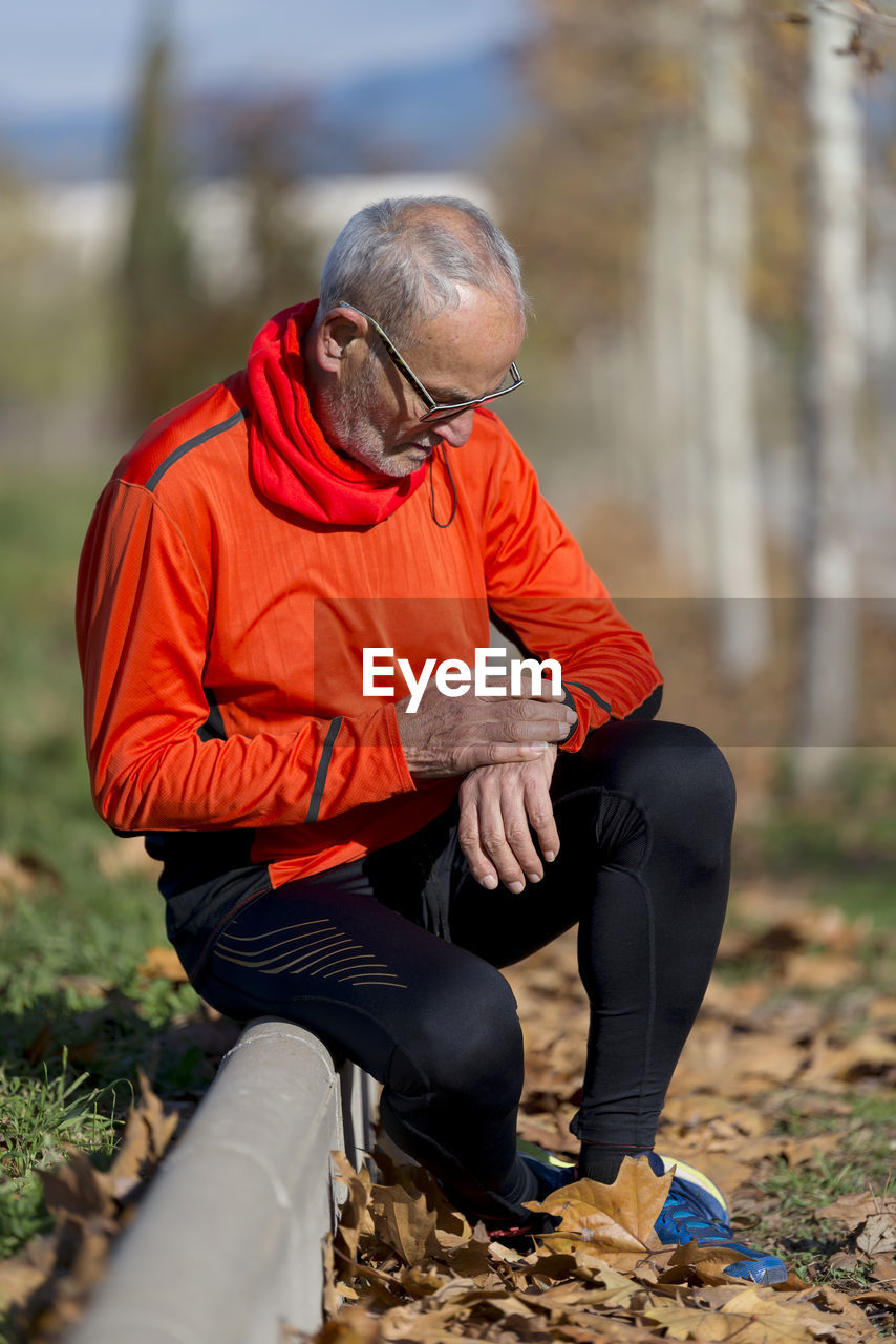 Senior man looking at wristwatch while sitting on curb