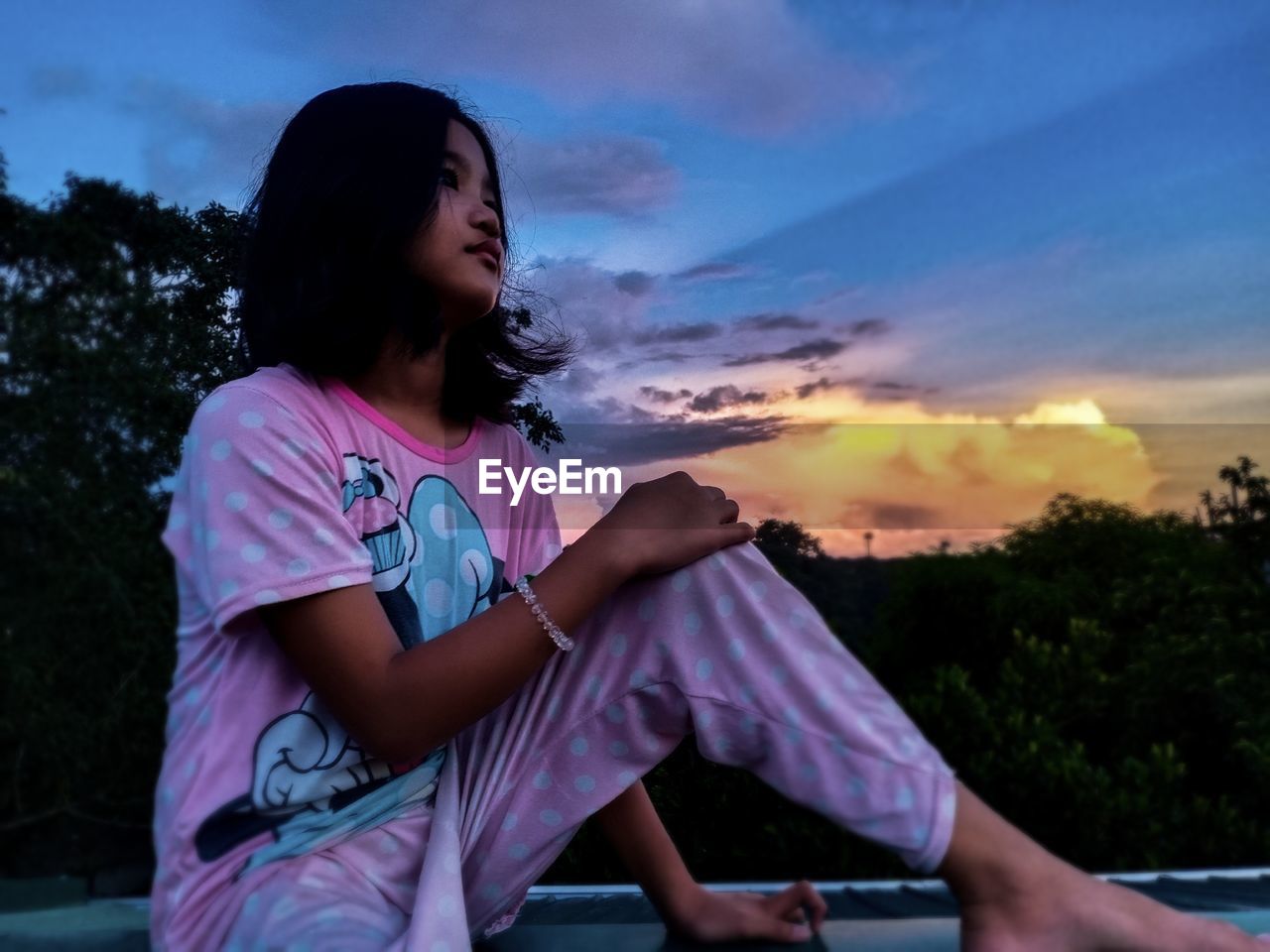 YOUNG WOMAN SITTING IN FRONT OF SKY