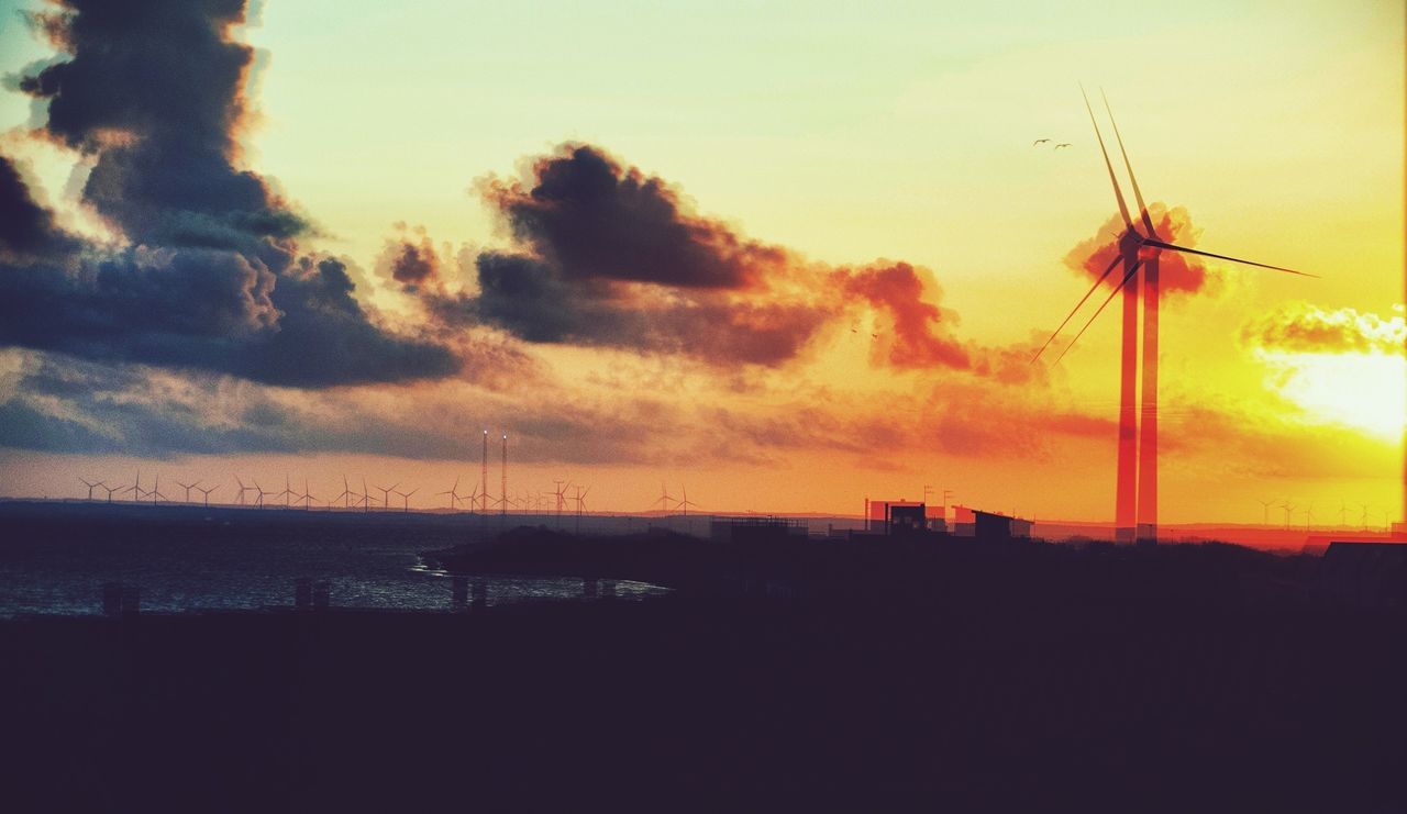 Wind turbine against cloudy sky during sunset