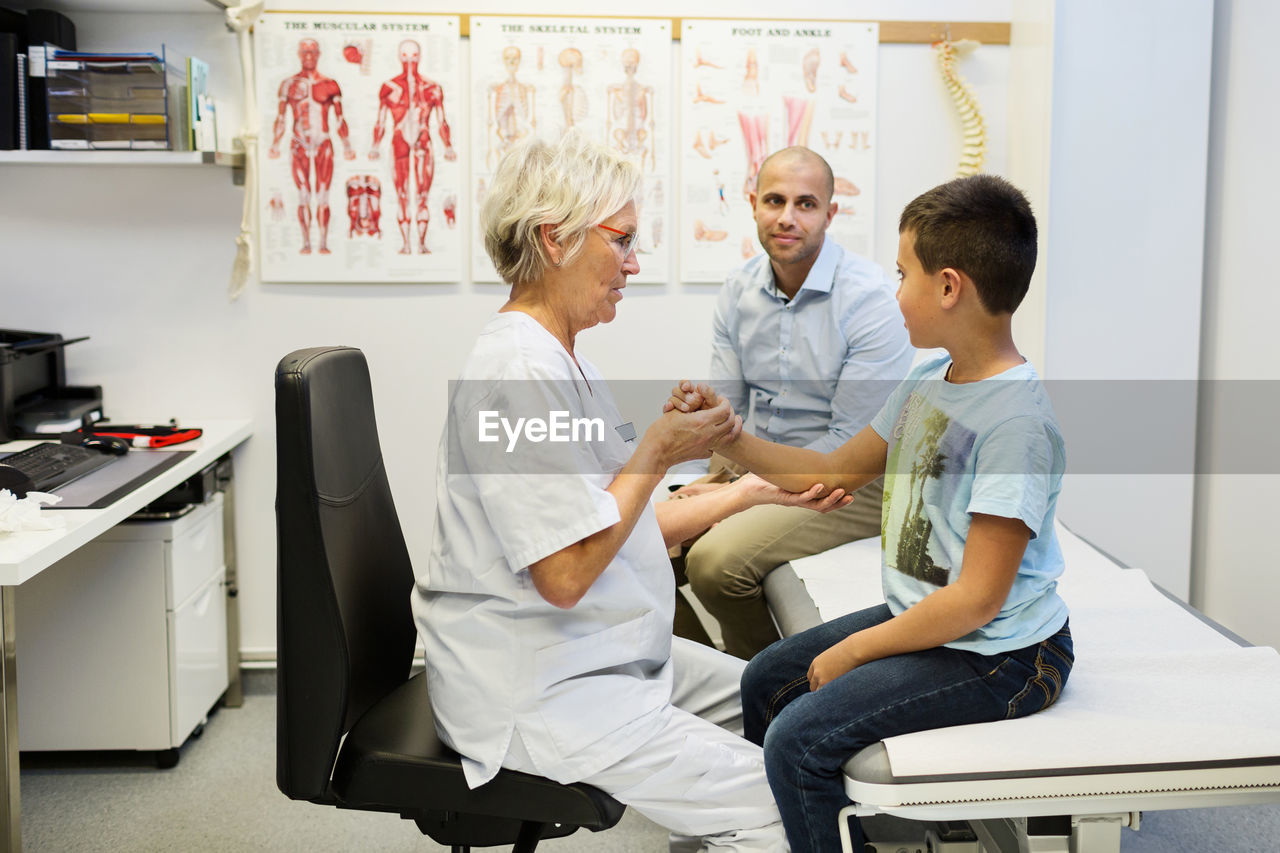 Father sitting by son being examined by orthopedic surgeon in clinic