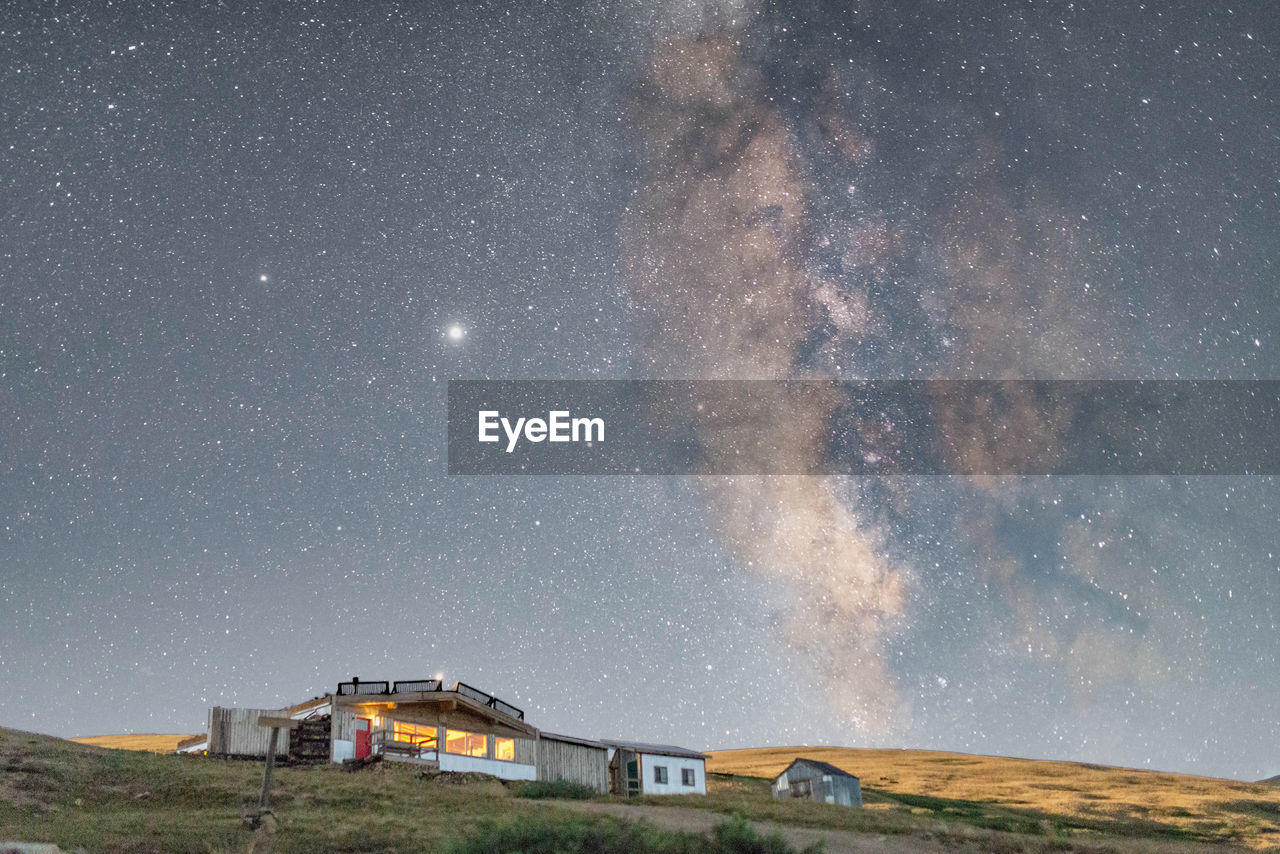View of cabin and field against starry sky at night