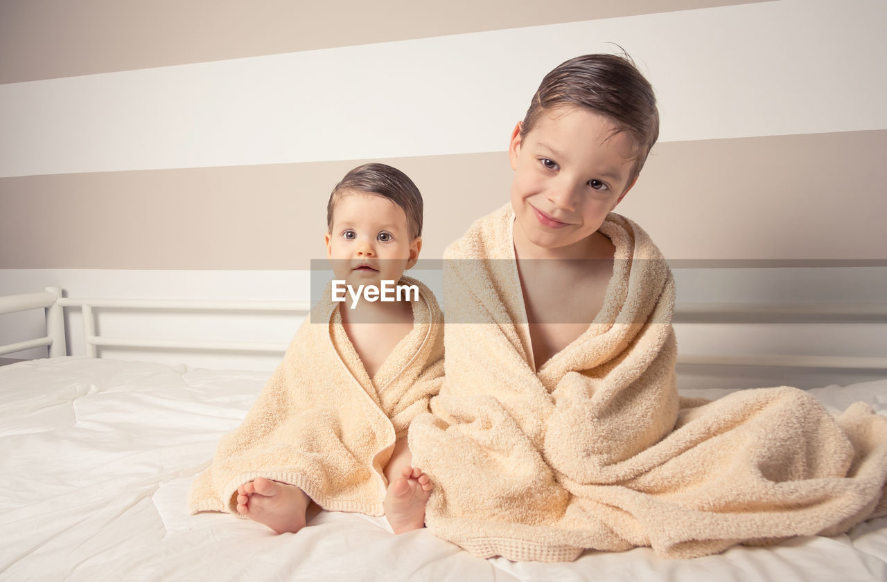 Cute shirtless siblings wrapped in towel against wall