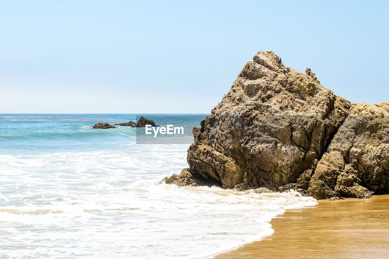 ROCK FORMATION ON BEACH AGAINST SKY