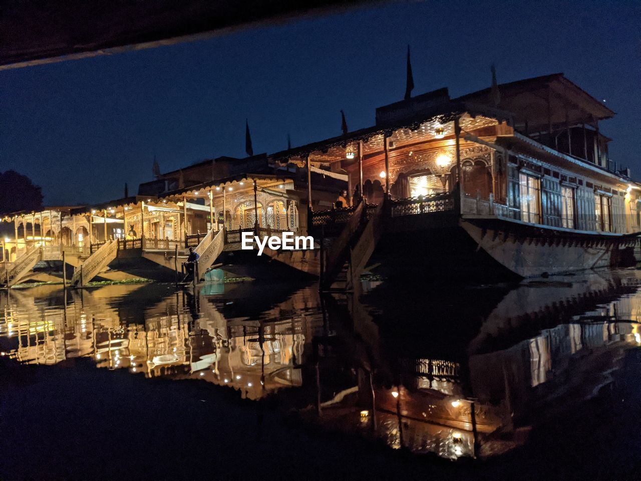 ILLUMINATED BUILDINGS BY RIVER IN CITY AGAINST SKY AT NIGHT