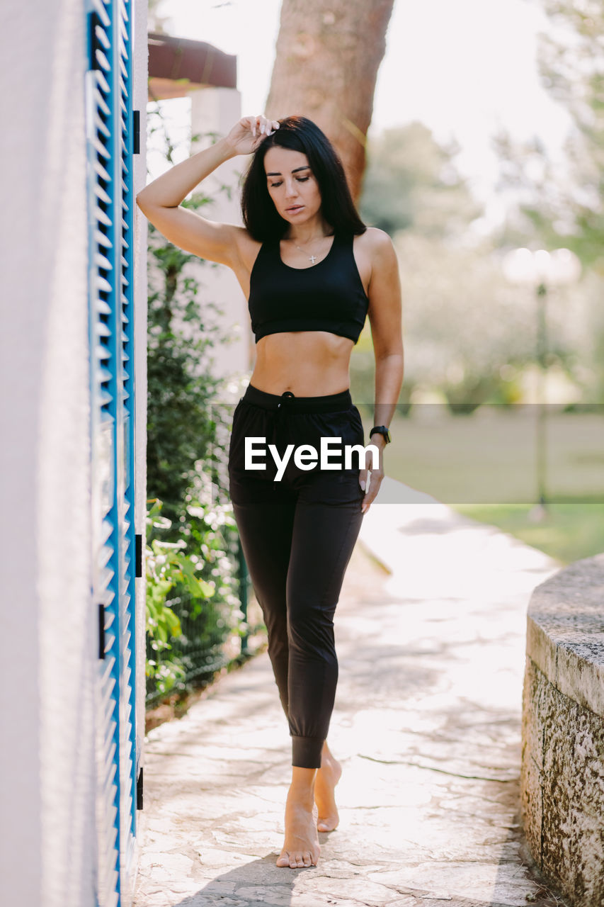 full length portrait of young woman standing on footpath