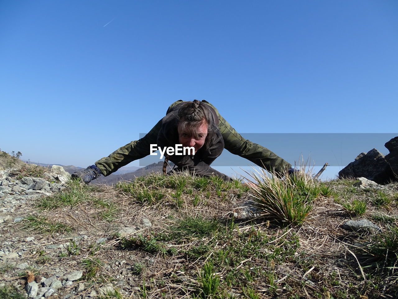 Woman stretching on mountain against clear sky