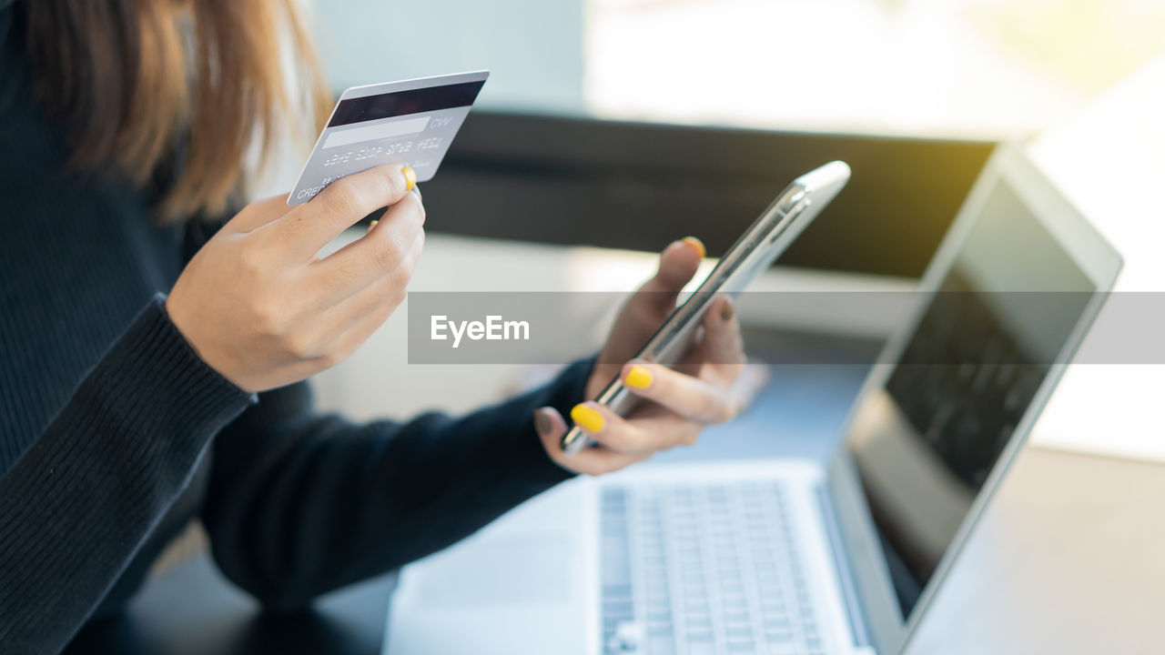 MIDSECTION OF WOMAN HOLDING SMART PHONE