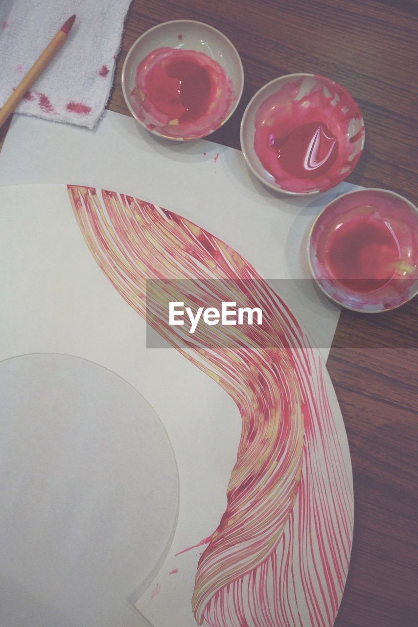 High angle view of red paint in bowl with painting on table