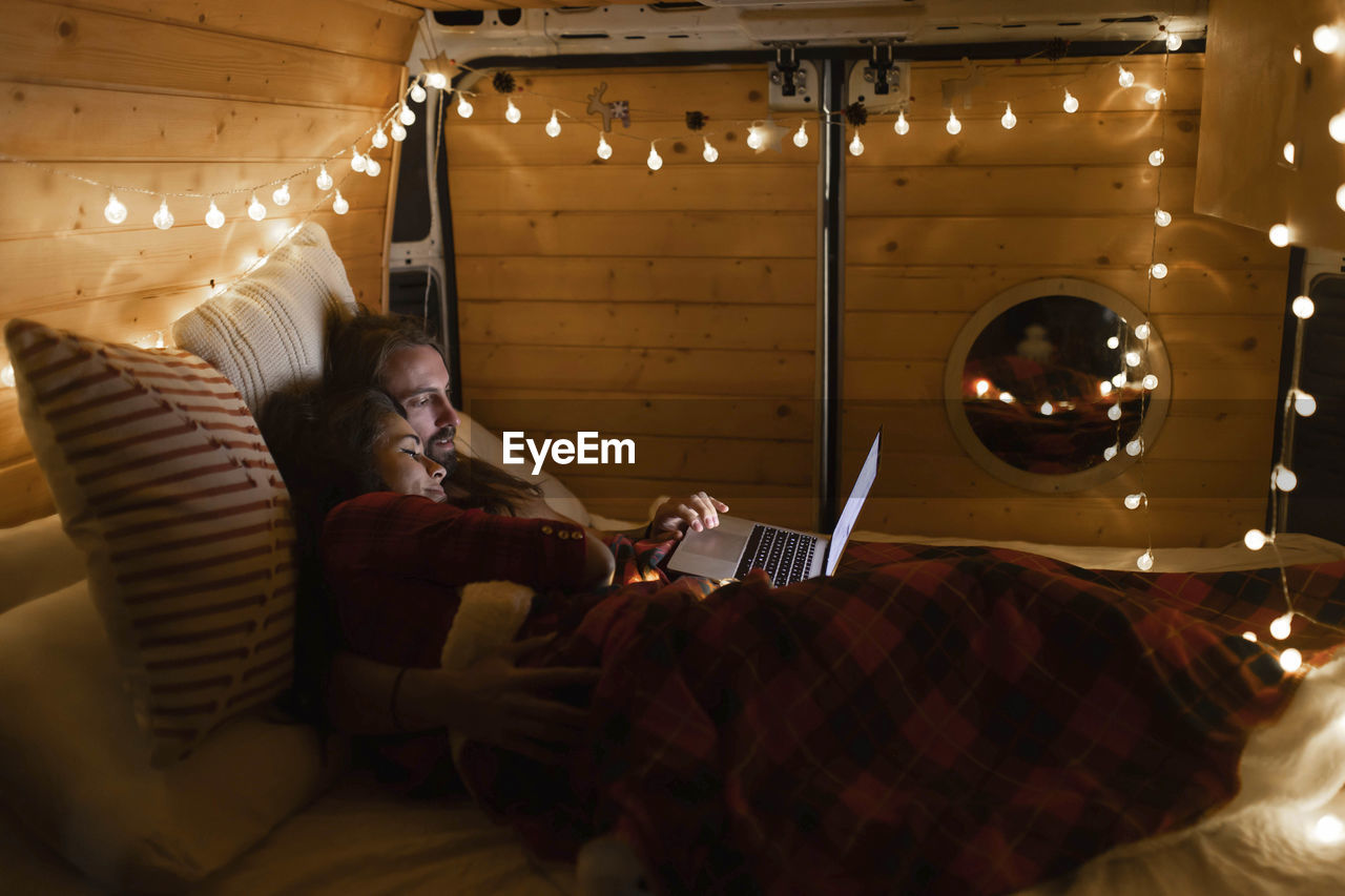 Young couple using laptop lying on bed in motor home