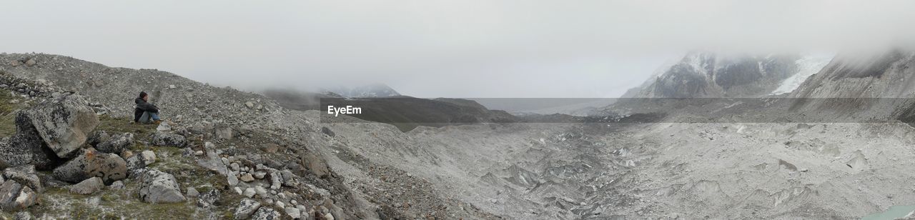 Panoramic view of mature man sitting on mountain against sky