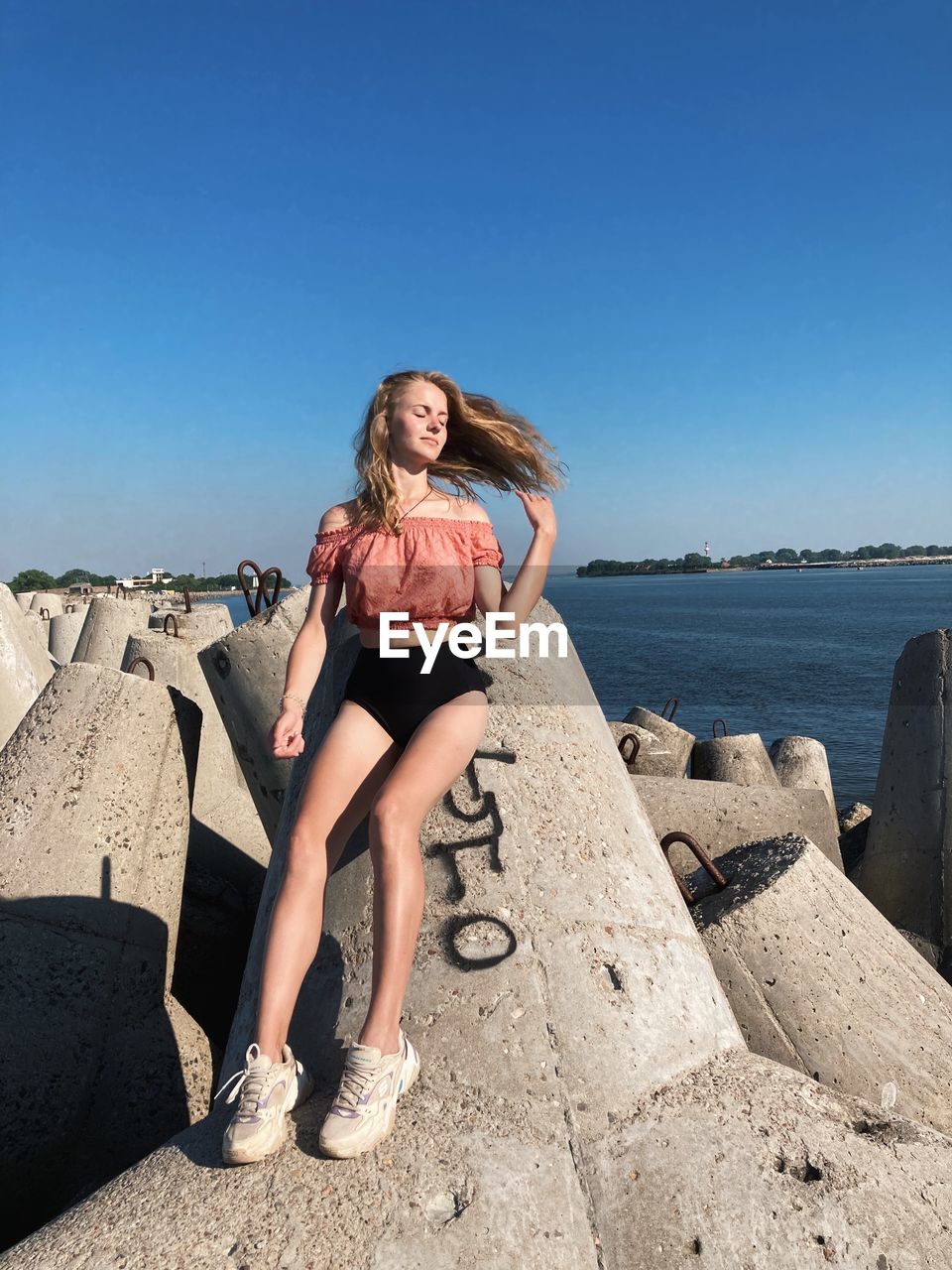 full length of young woman sitting on rock at beach