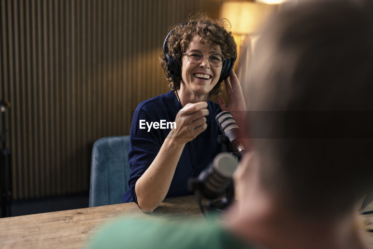 Happy presenter wearing eyeglasses talking with guest in radio station