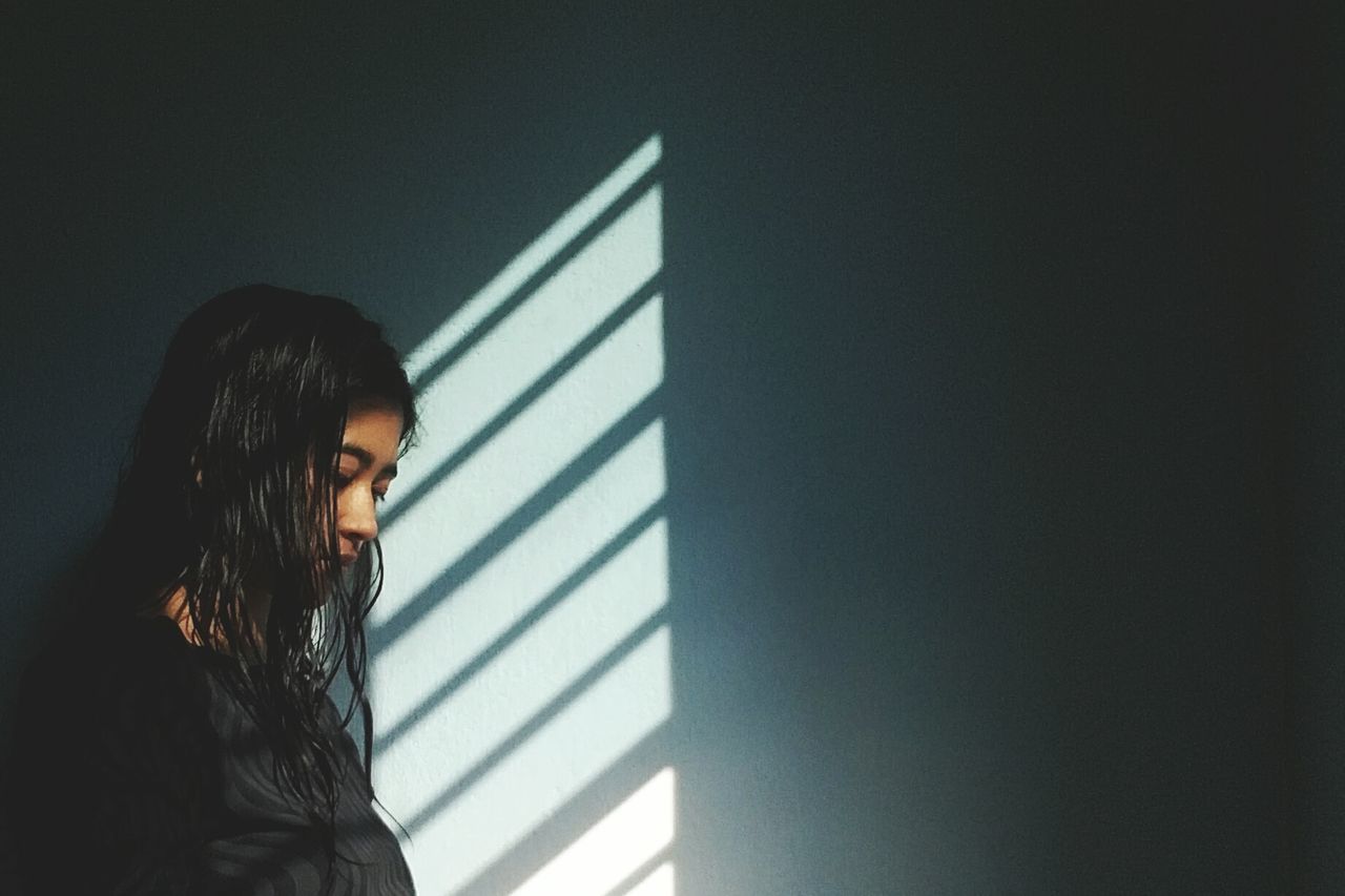 Side view of thoughtful young woman standing by wall at home