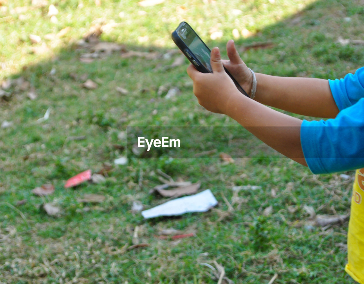 MIDSECTION OF CHILD HOLDING CAMERA ON FIELD