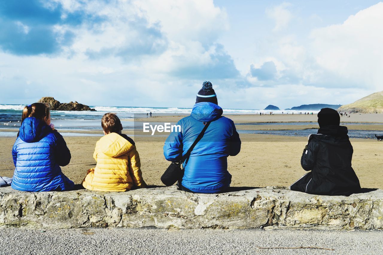 Rear view of people sitting at beach against sky