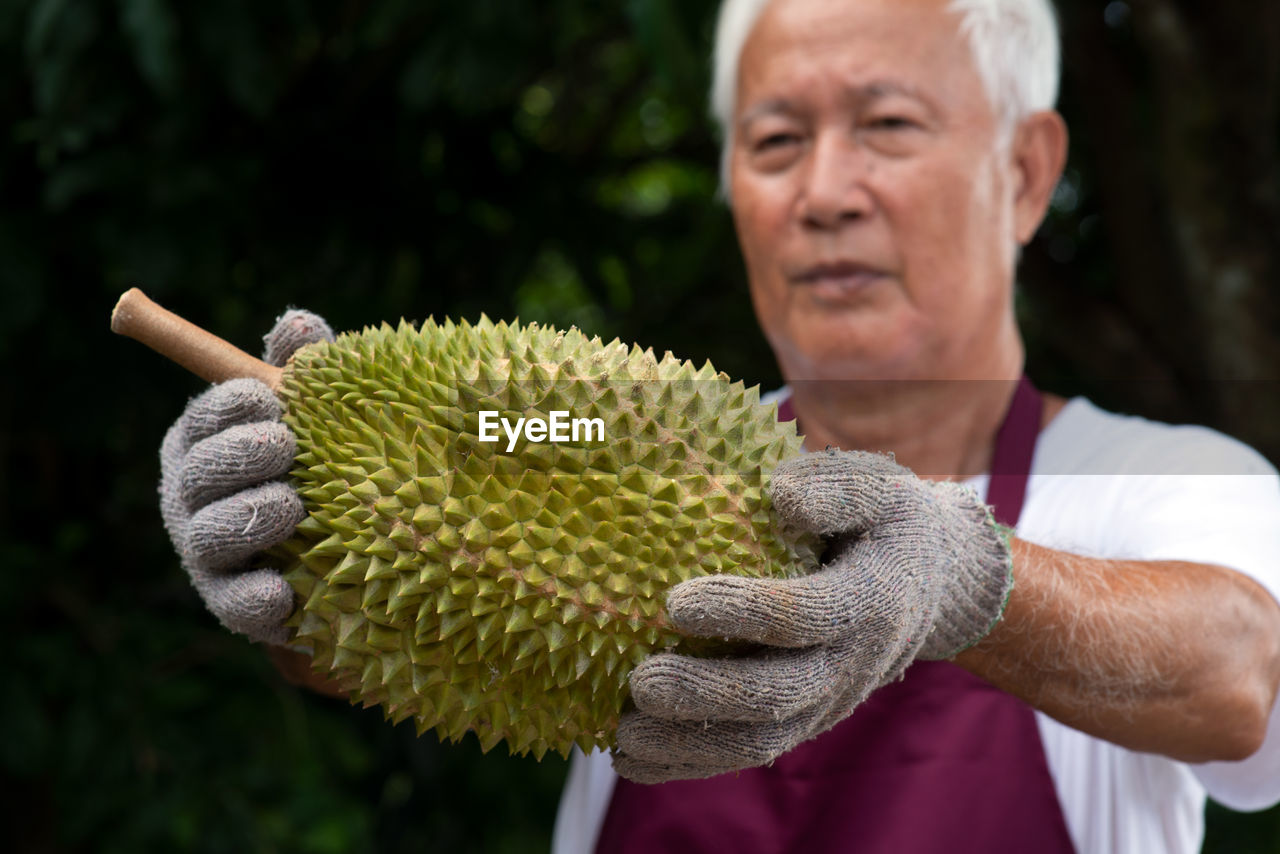 Midsection of man holding durian while standing against trees