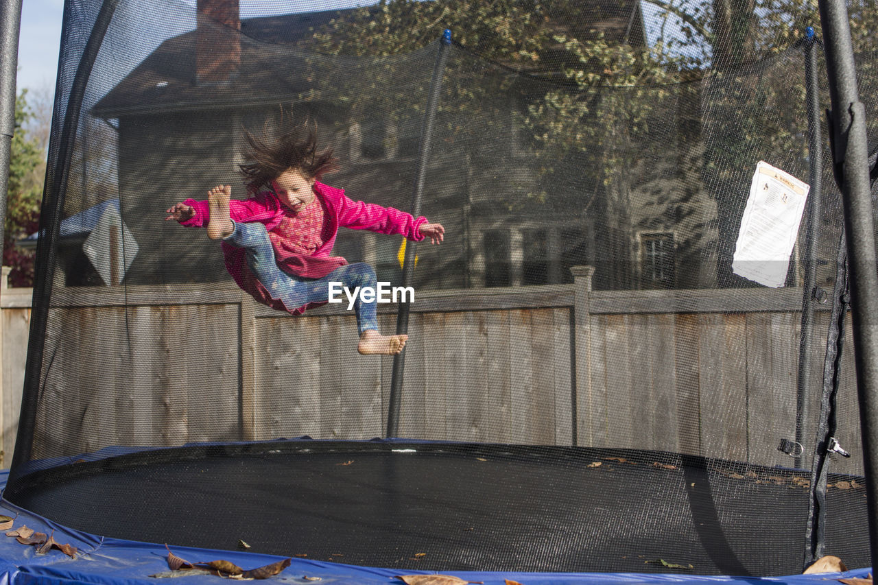 A joyful little girl with wild hair jumps on trampoline with mesh net