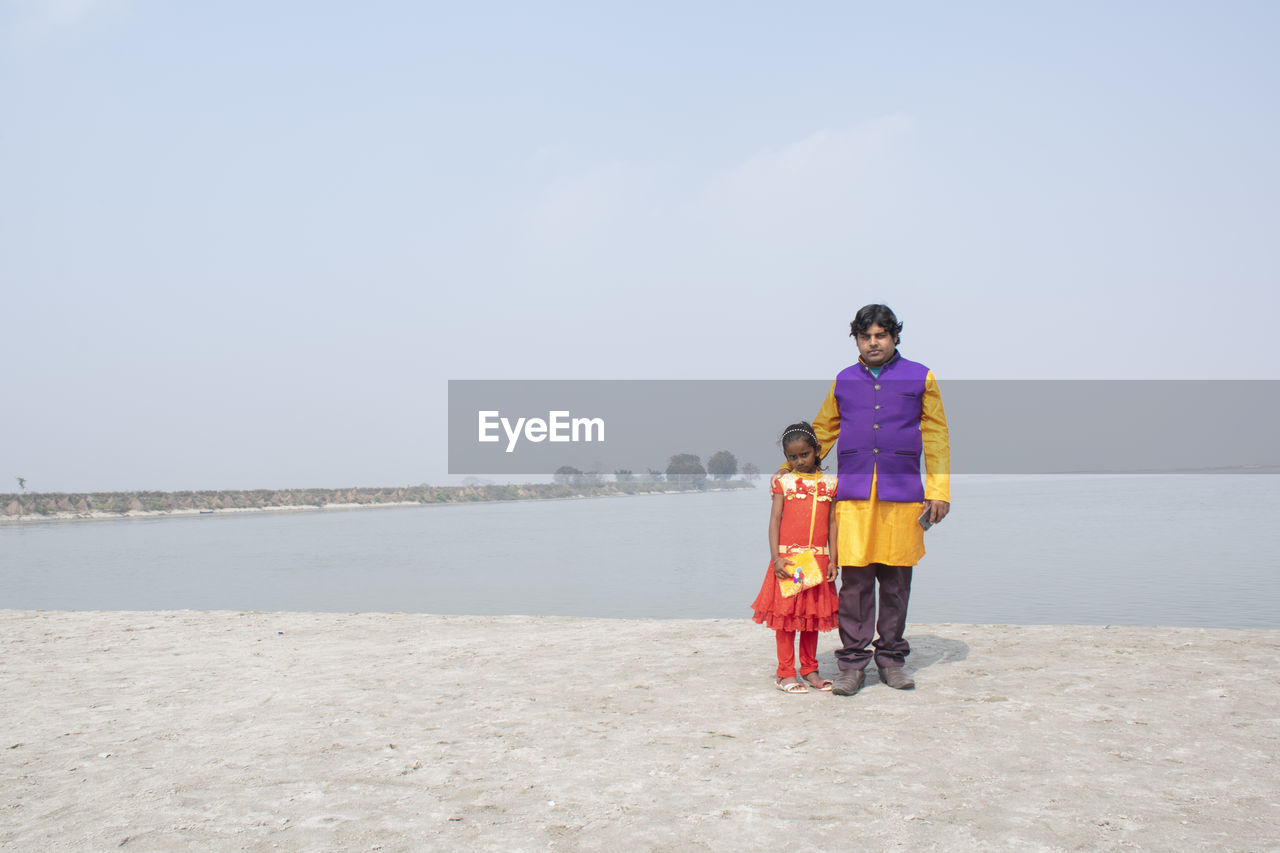 Full length portrait of father with daughter standing against sea and sky