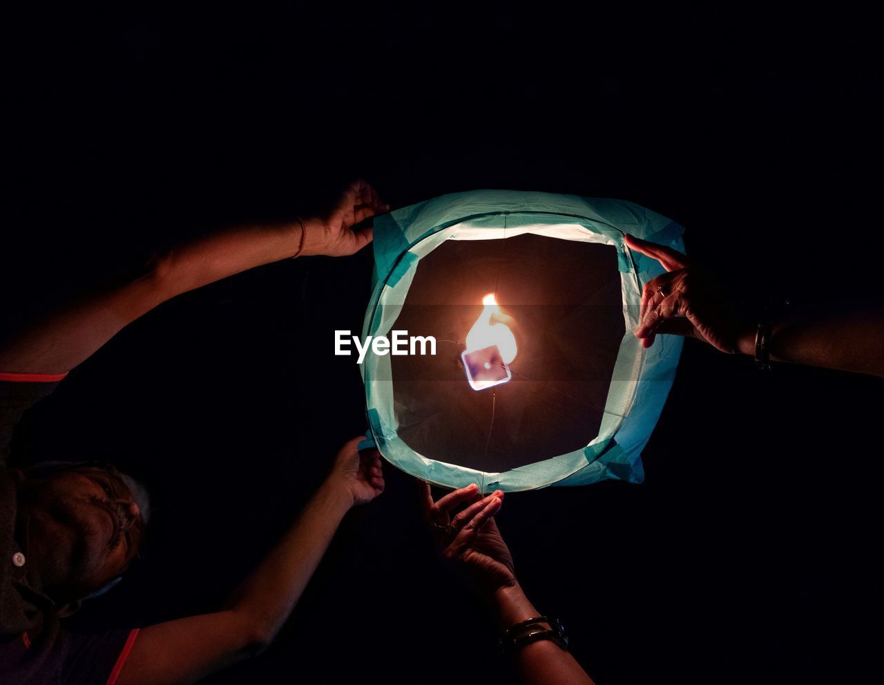 Close-up of hand holding lit paper / sky lantern against black background on diwali
