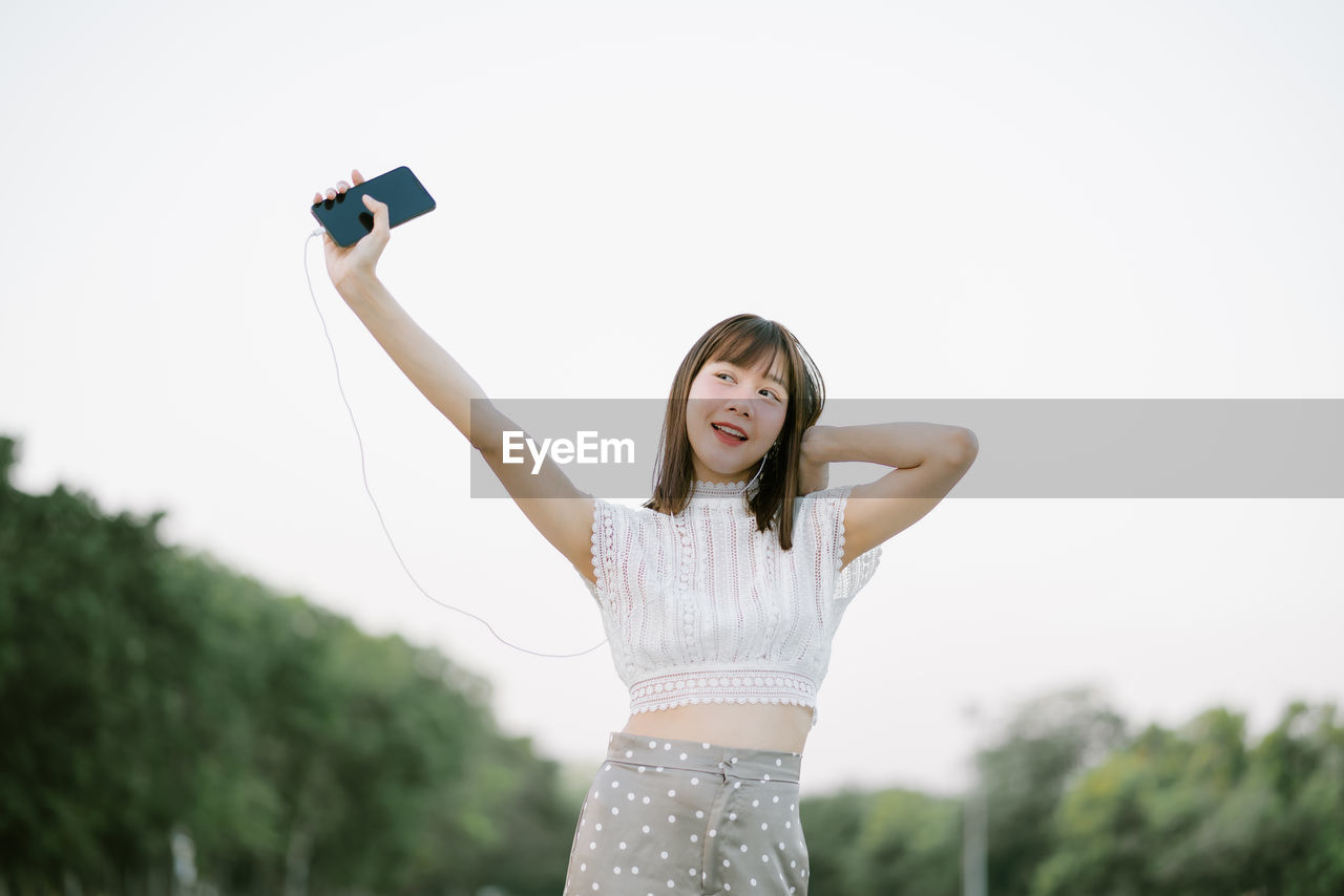 Young woman holding smart phone and looking away while standing on land