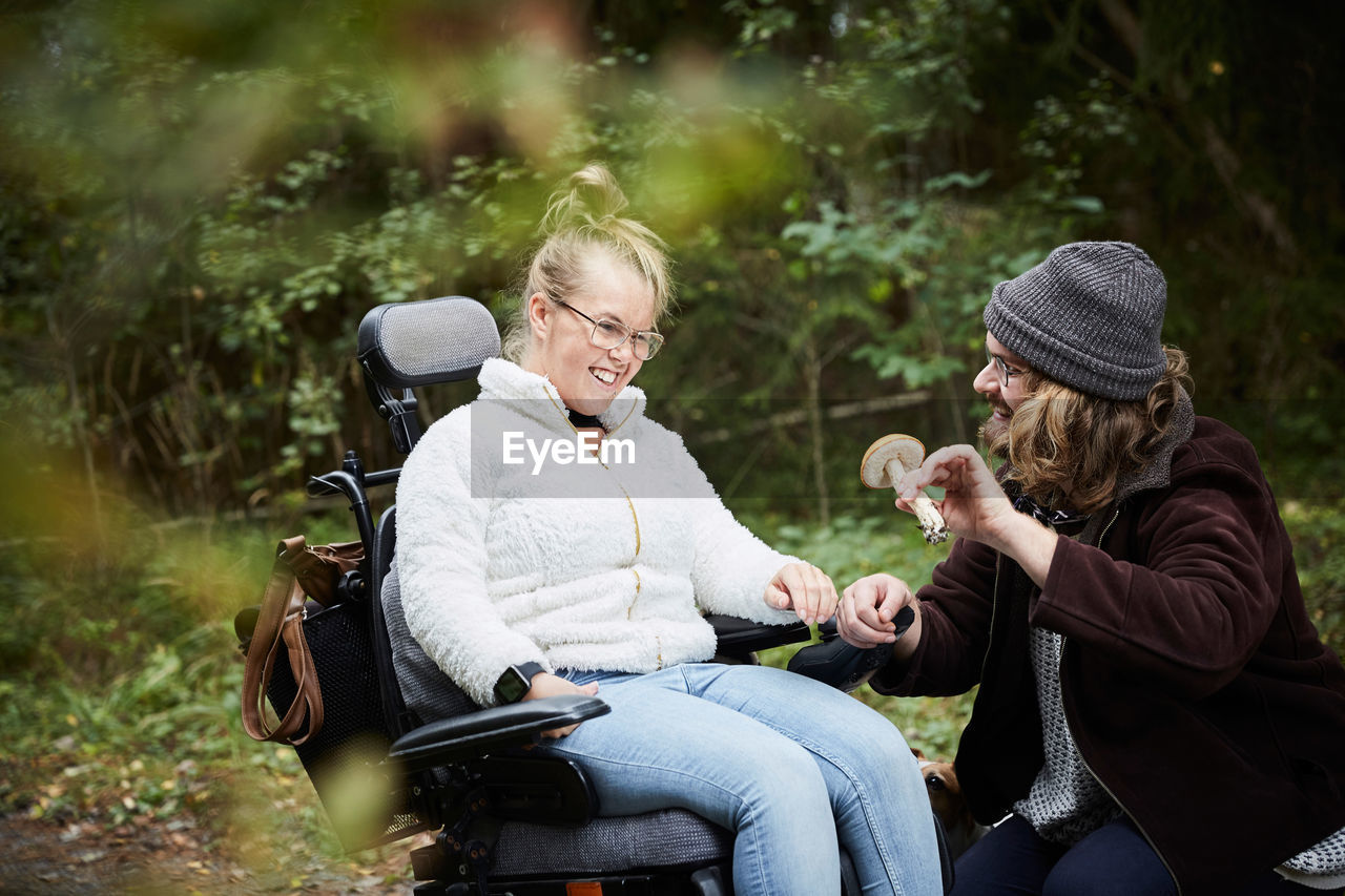 Male caretaker showing mushroom to disabled woman in wheelchair at forest