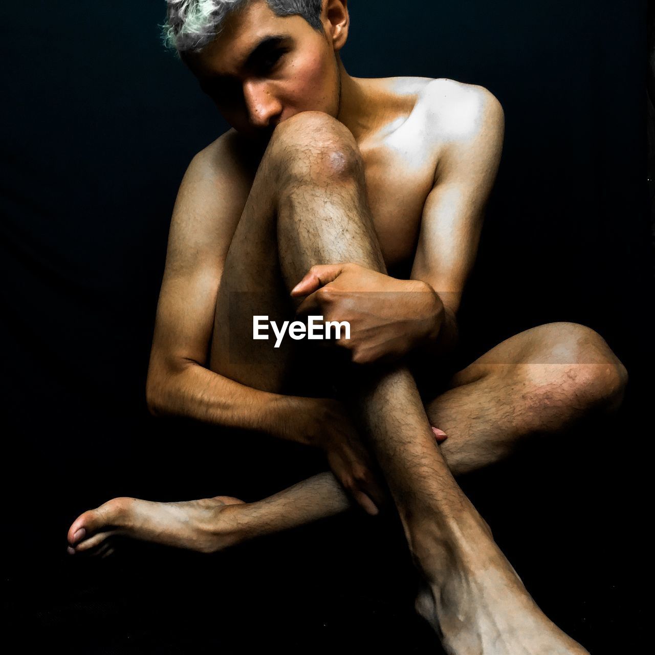 Full length of shirtless man sitting against black background