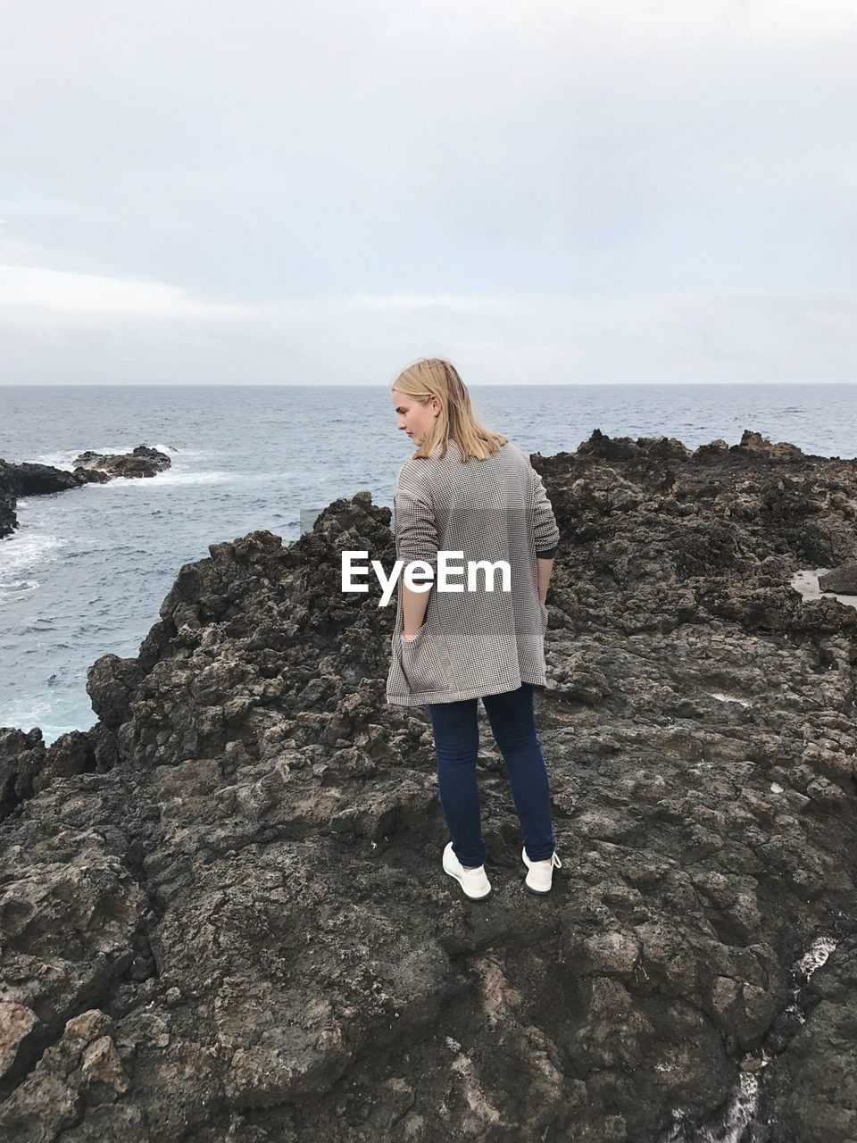 Woman standing on rock formation by sea against sky