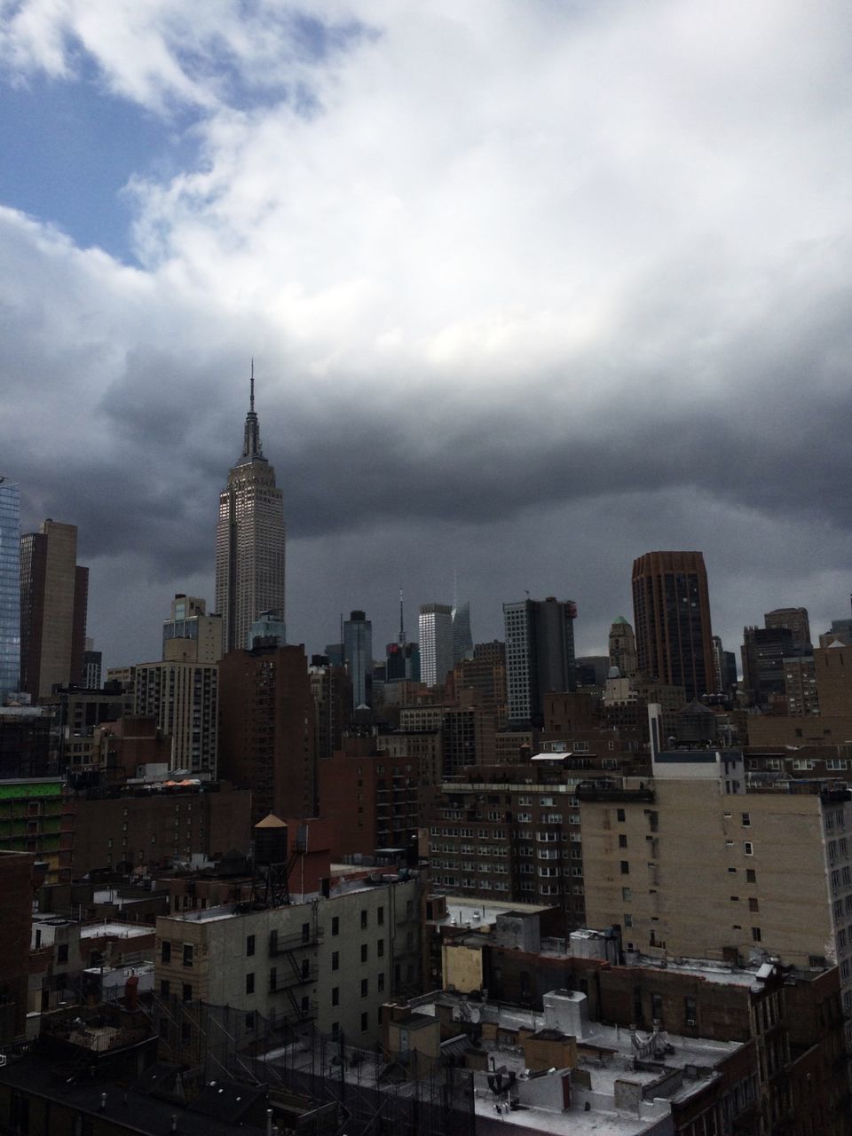 Low angle view of empire state building amidst towers against cloudy sky