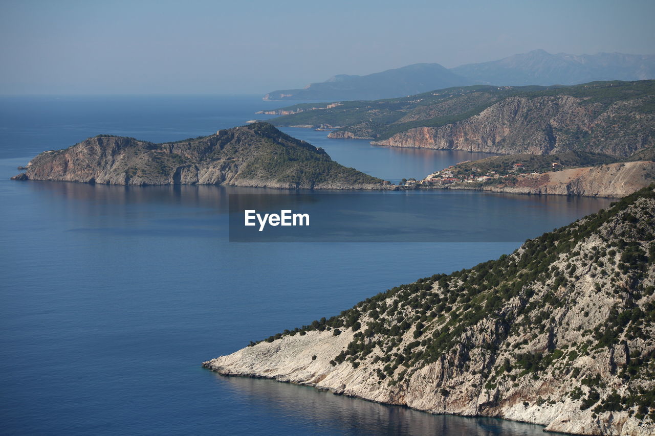 Scenic view of sea by mountains against clear blue sky